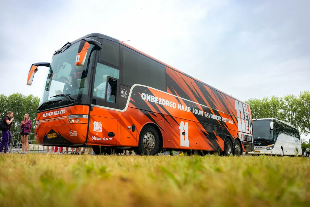 Oranje touringcar van Eleven Travel met de tekst Onbezorgd naar jouw favoriete festival