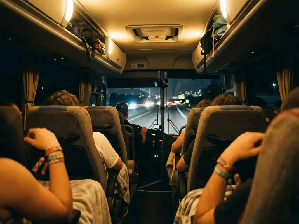 Tourbus met festivalgangers die slapen en praten in comfortabele stoelen, kleurrijke polsbandjes zichtbaar, nachtelijke rit
