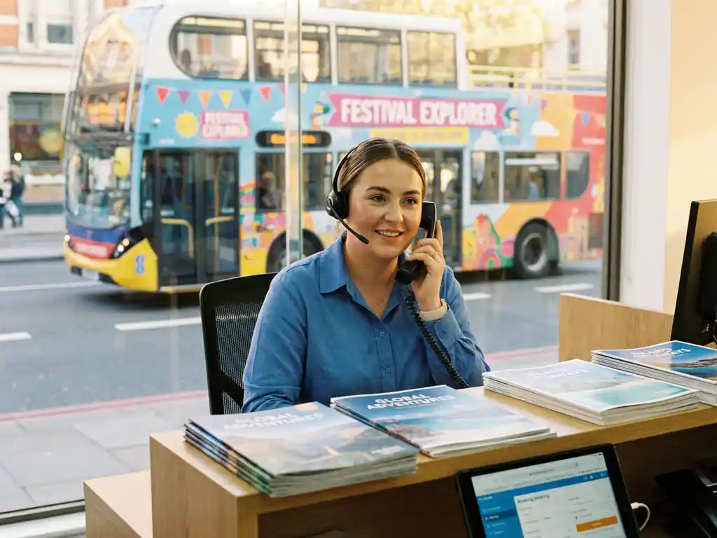 Vriendelijke klantenservice medewerker met headset beantwoordt telefoontje aan bureau met reisbrochures