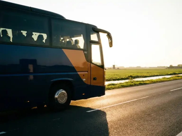 Luxe touringcar op Nederlandse snelweg tijdens gouden uur, met festivalgangers zichtbaar door getinte ramen en vlak polderlandschap op achtergrond.