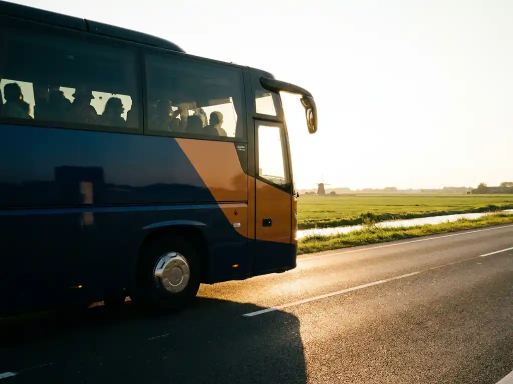 Luxe touringcar op Nederlandse snelweg tijdens gouden uur, met festivalgangers zichtbaar door getinte ramen en vlak polderlandschap op achtergrond.
