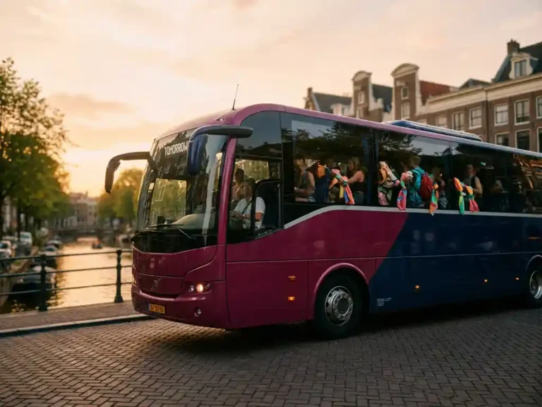 Luxe touringcar met Tomorrowland-festivalgangers vertrekt bij gouden uur van een Amsterdamse keistraat langs een gracht.